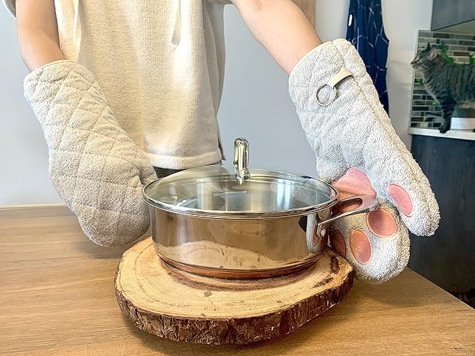 A woman wearing a pair of paw designed oven mitts on top of a pot.