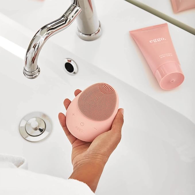 A person holding a pink facial cleansing device in a sink.