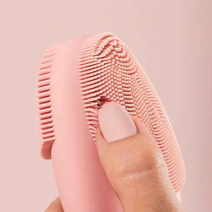 A person holding a pink facial cleansing device.