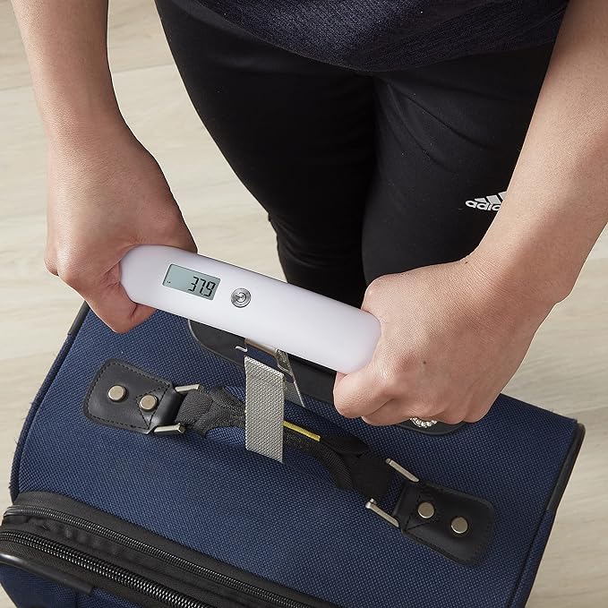 A person holding a luggage scale with a digital thermometer, preparing for travel.