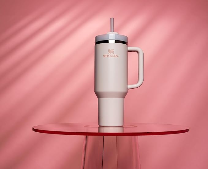 A white mug tumbler with a straw sitting on top of a pink background.